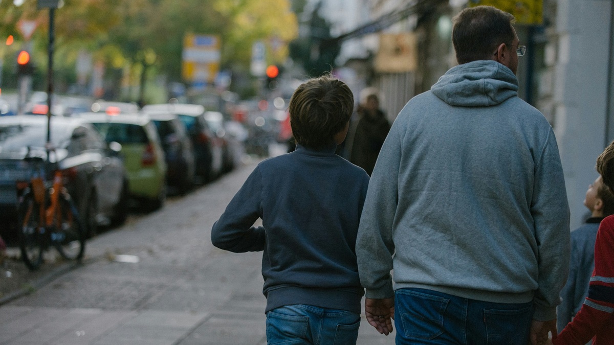 An adult and a child walking together along a city street, seen from behind.